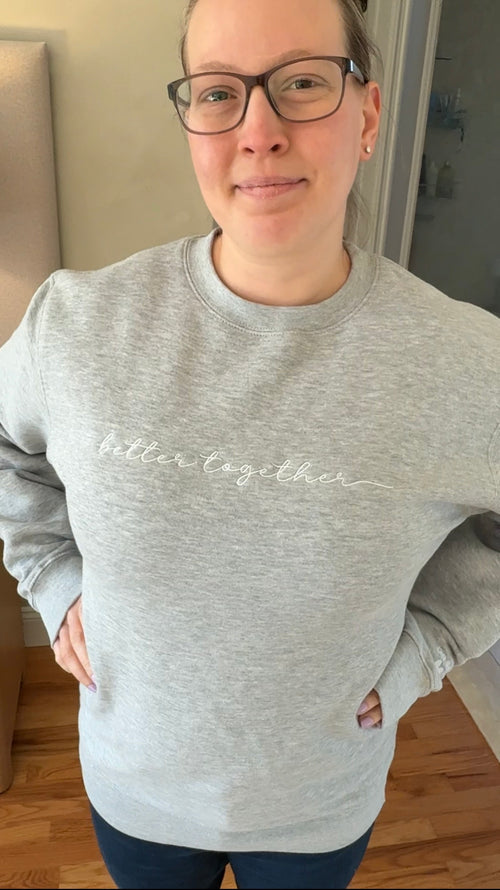 Heather grey sweatshirt with 'better together' text in white embroidery across center front worn by a person