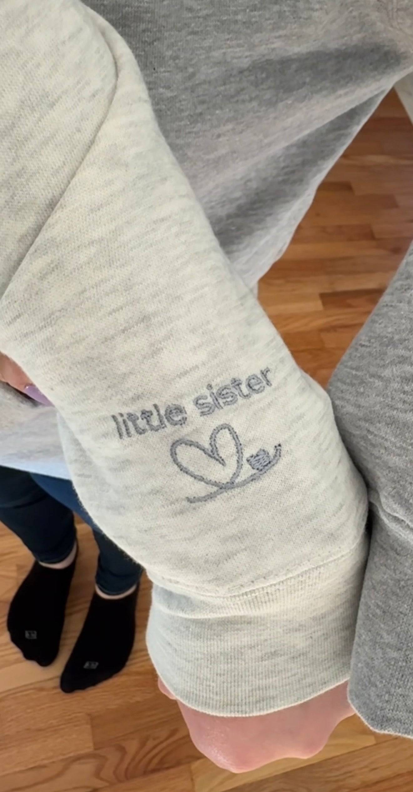 Heather oatmeal sweatshirt with 'little sister' text in grey embroidery on the left sleeve